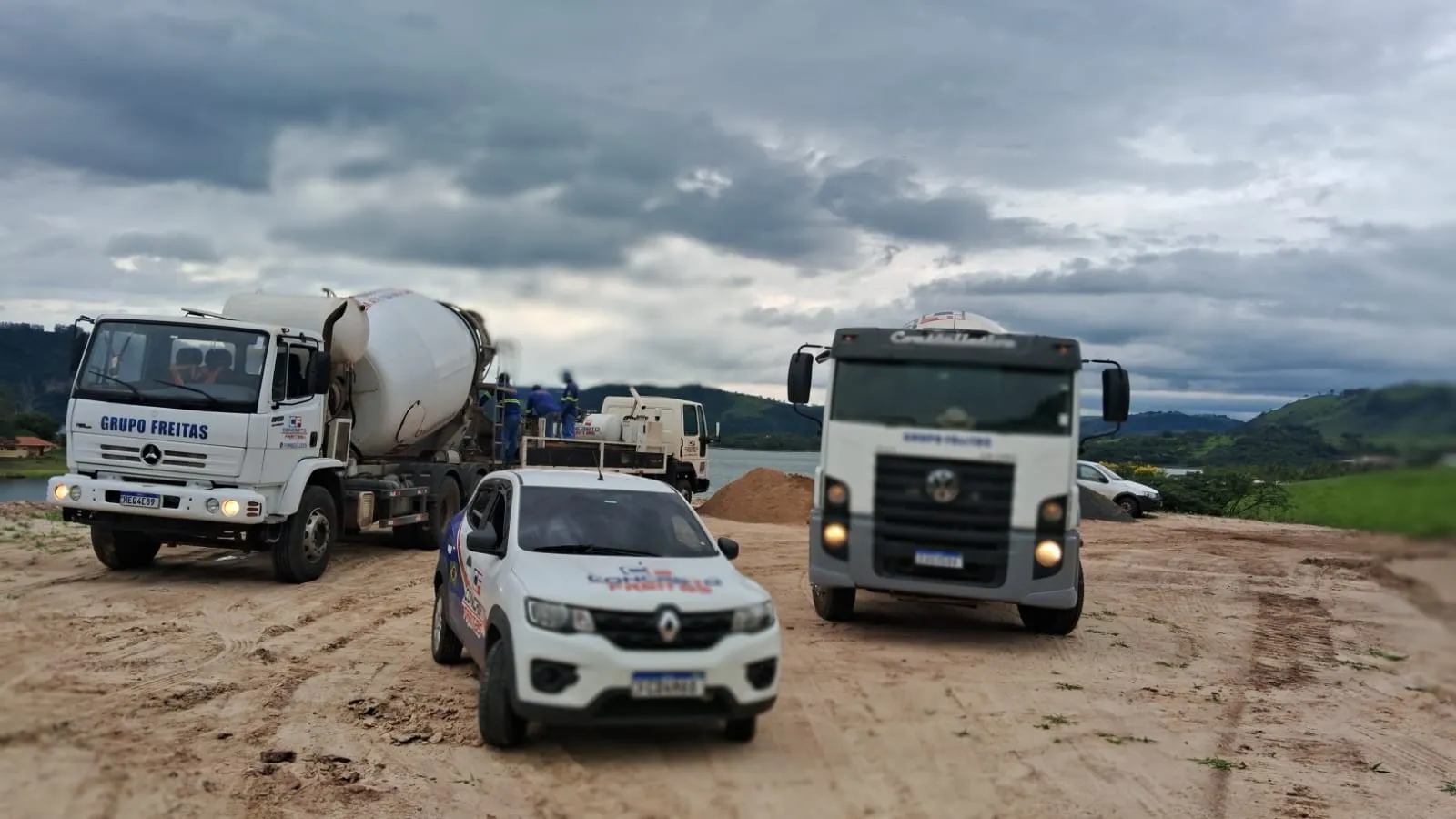 Veículo de atendimento e caminhões betoneira da Concreto Freitas em uma obra à beira de um lago