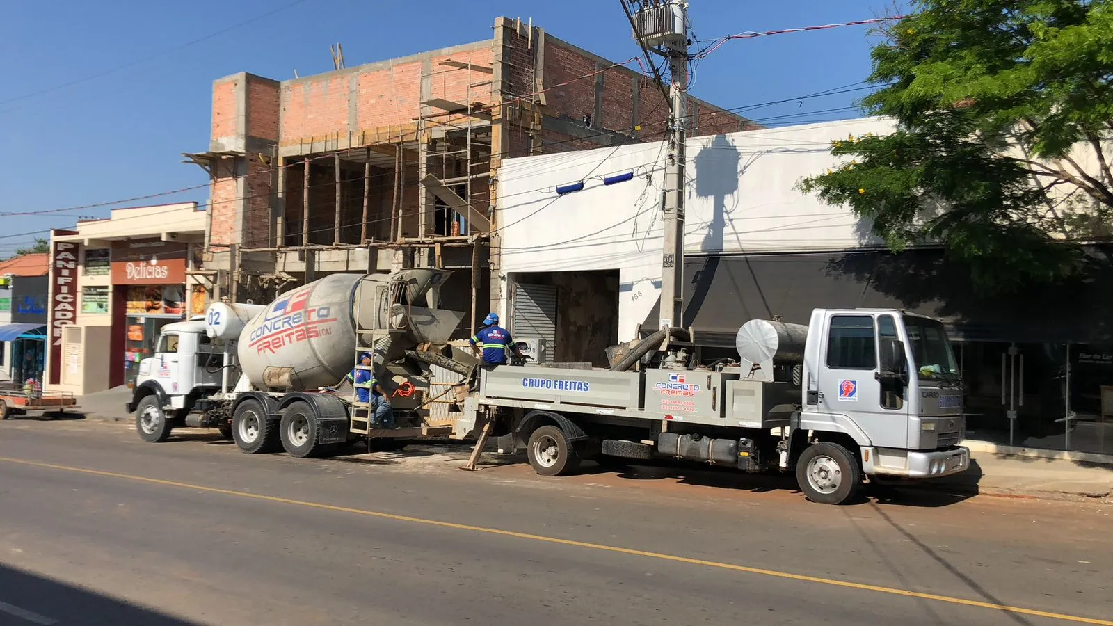 Caminhão betoneira e bomba de concreto operando na rua em frente a uma obra