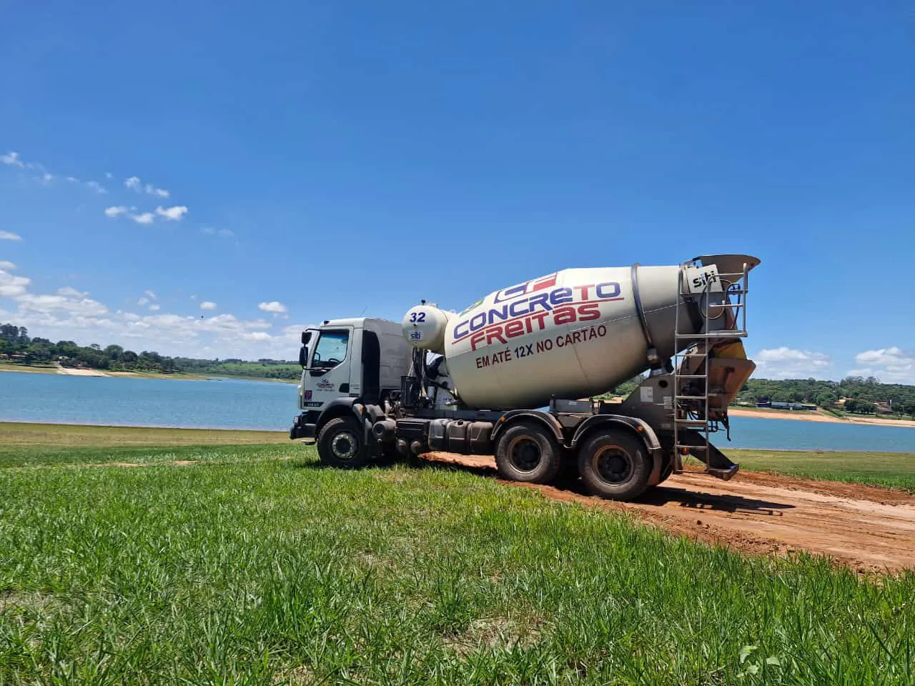 Caminhão betoneira da Concreto Freitas em obra às margens de um lago, em meio à paisagem aberta da região