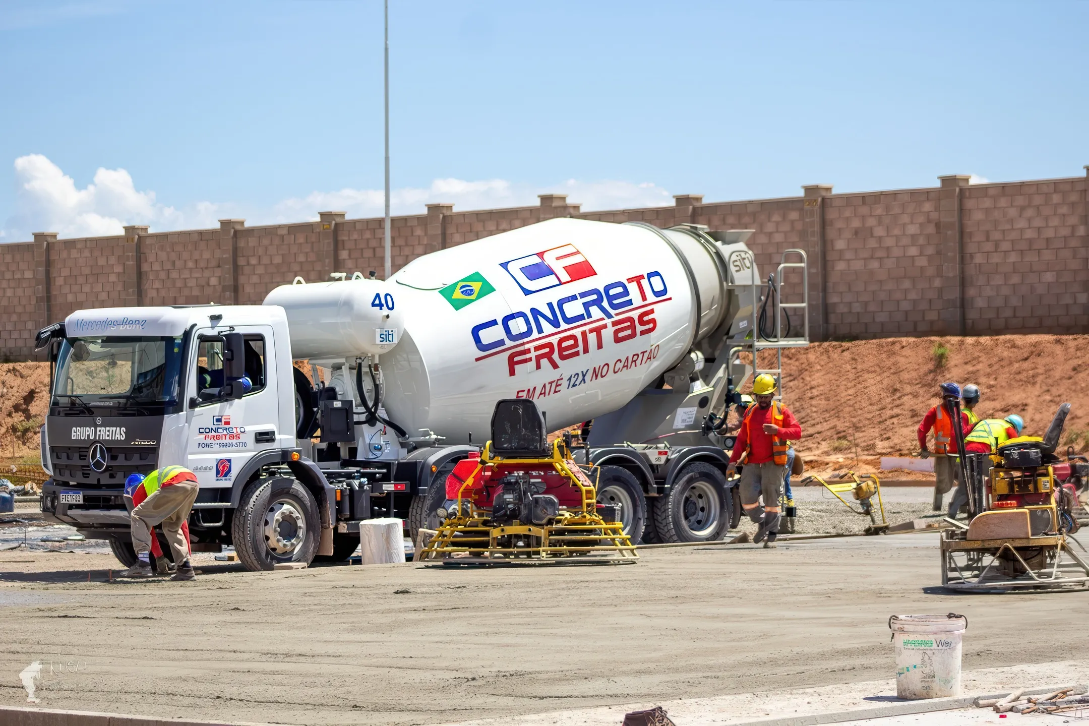 Caminhão betoneira da Concreto Freitas ao lado da equipe que acaba um piso de concreto com máquinas alisadoras
